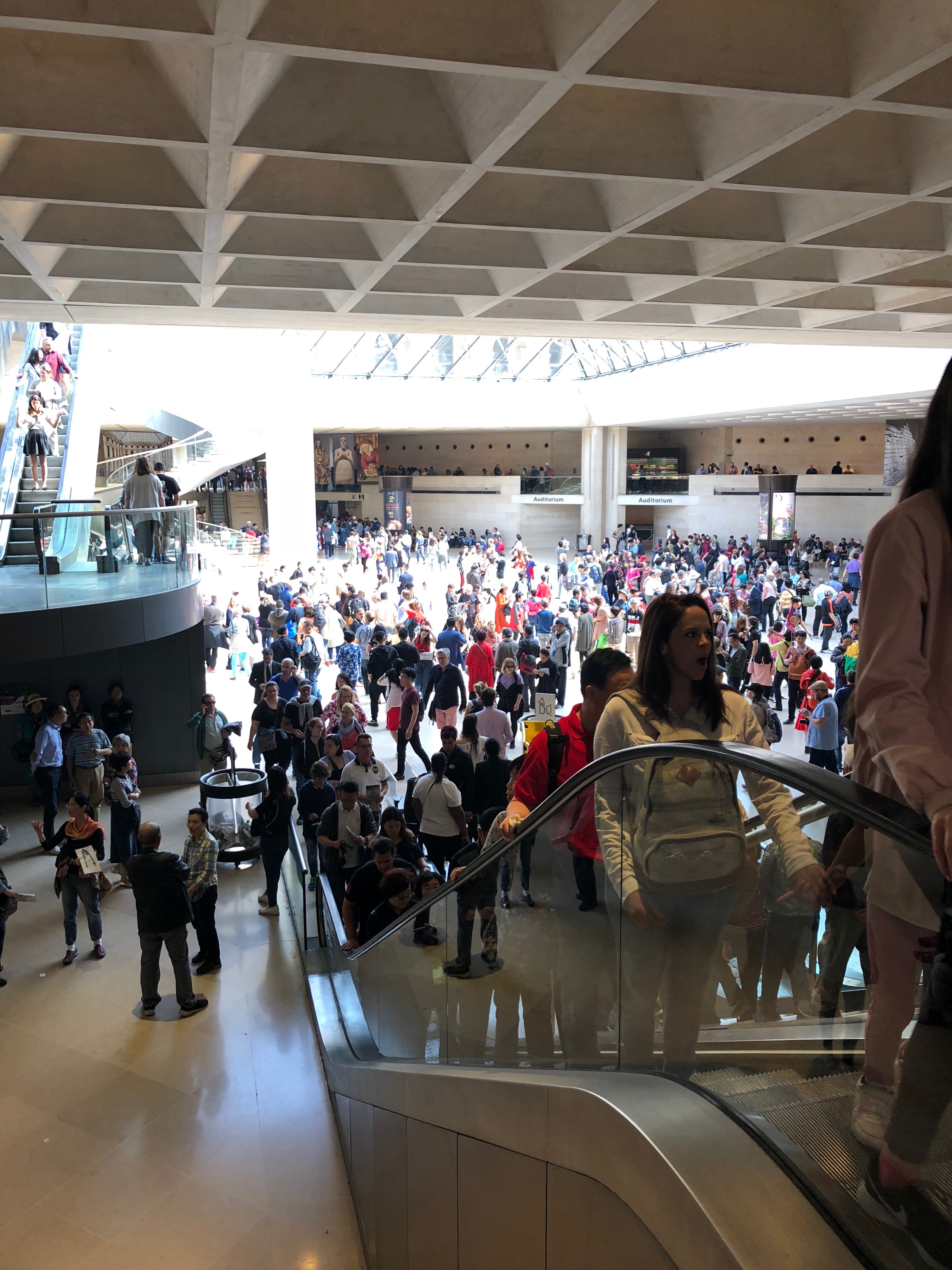 Crowds of people at the Louvre ascend an escalator. 