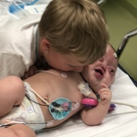 Little baby with disabilities in hospital bed, brother is leaning over and kissing her