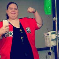 woman taking a selfie in a mirror next to her IV stand and flexing her bicep, and a large bruise