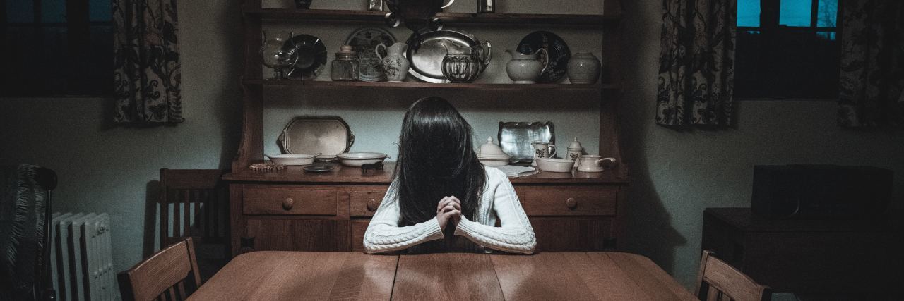 When Depression Is an Uninvited Houseguest woman sitting at table in dark room with hair hiding face