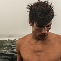 man at seaside topless looking down cloudy weather