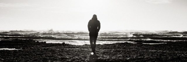 man at shore silhouetted against sky in black and white