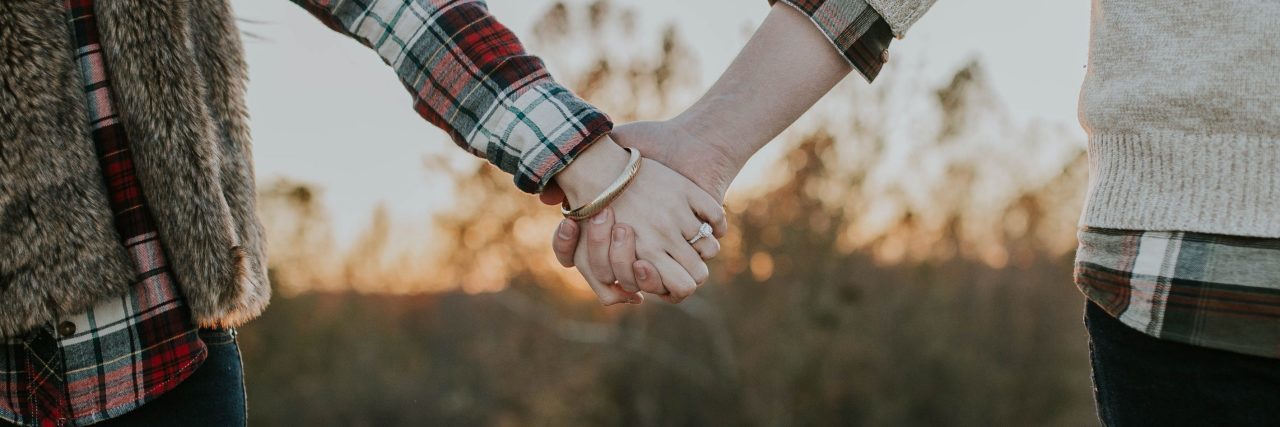 What It's Like to Be in a Relationship When Both Have a Mental Illness couple holding hands at sunset in front of field