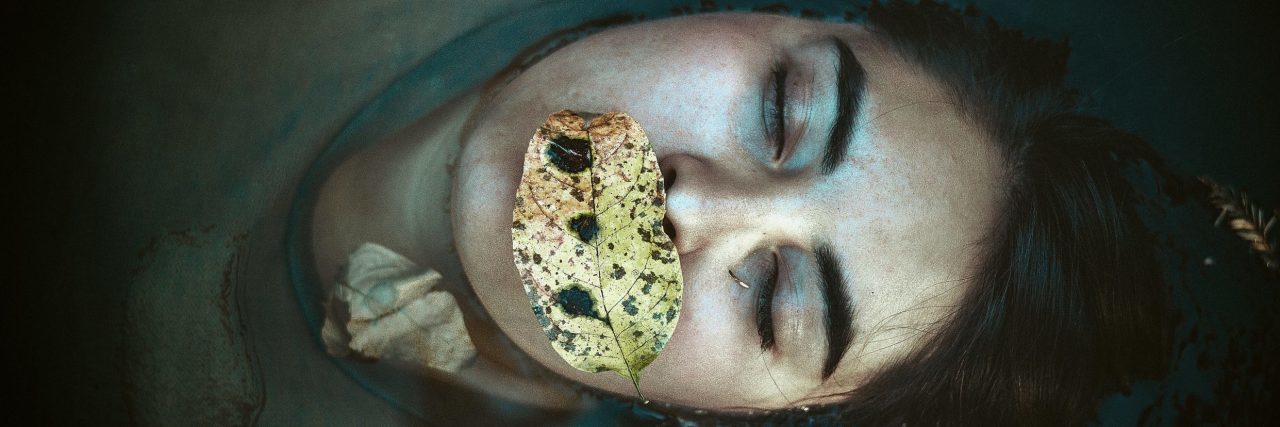 woman lying on back in water with eyes closed and leaf on mouth