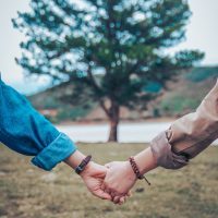 two people holding hands in front of large tree