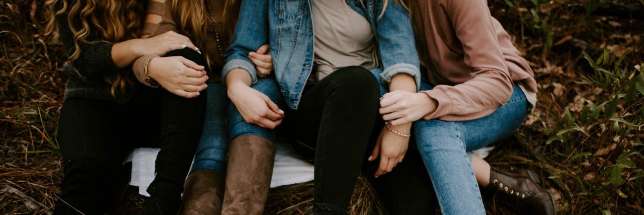 Tips for a Healthy Friendship When You Both Have a Mental Illness close up on group of friends sitting on ground close to each other and holding hands