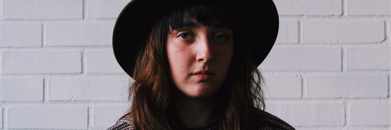 Don't Say 'Everything Happens for a Reason' to Sexual Assault Survivor woman in hat sitting in front of white brick wall