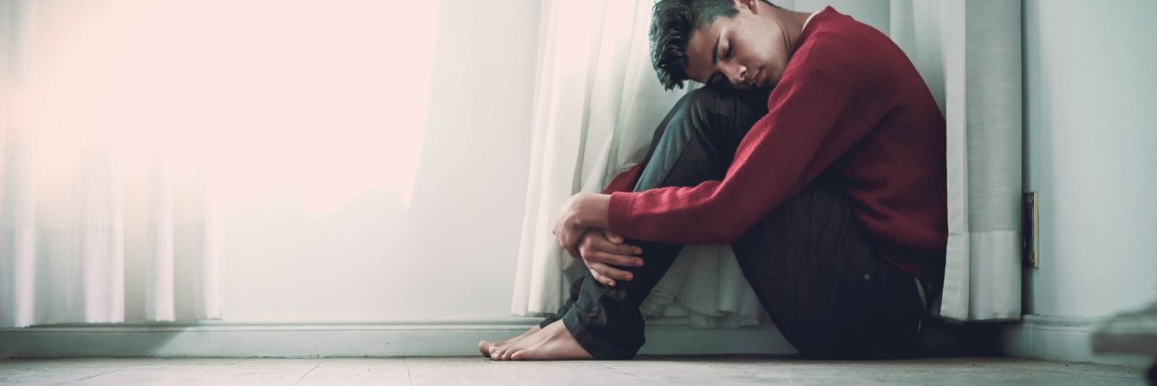 'Secret' Ways to Manage Social Anxiety young man sitting on floor under window hugging knees