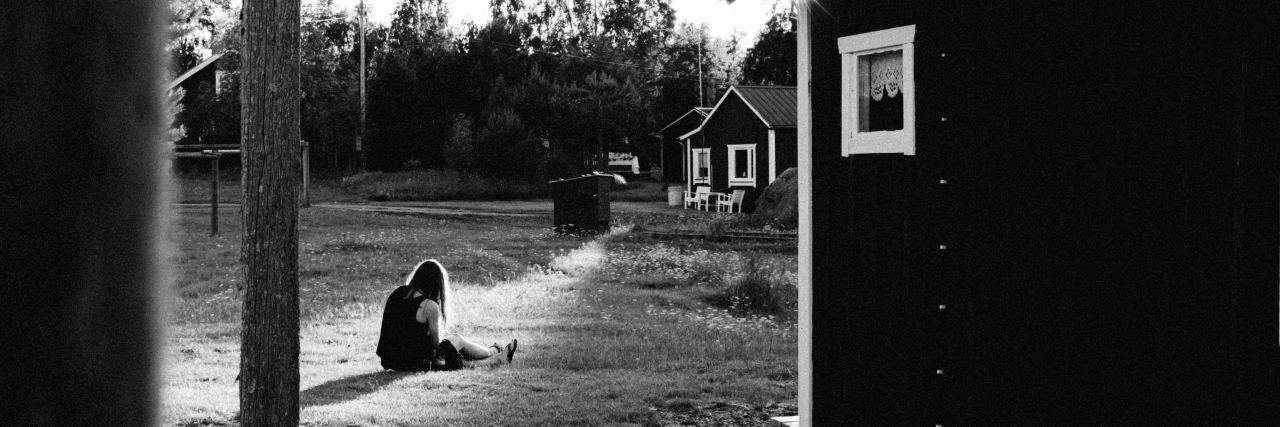black and white photo of girl sitting outside cabin on ground