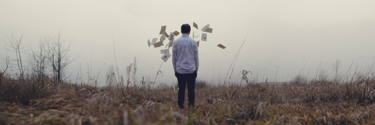 man facing away from camera in field having thrown pages into air