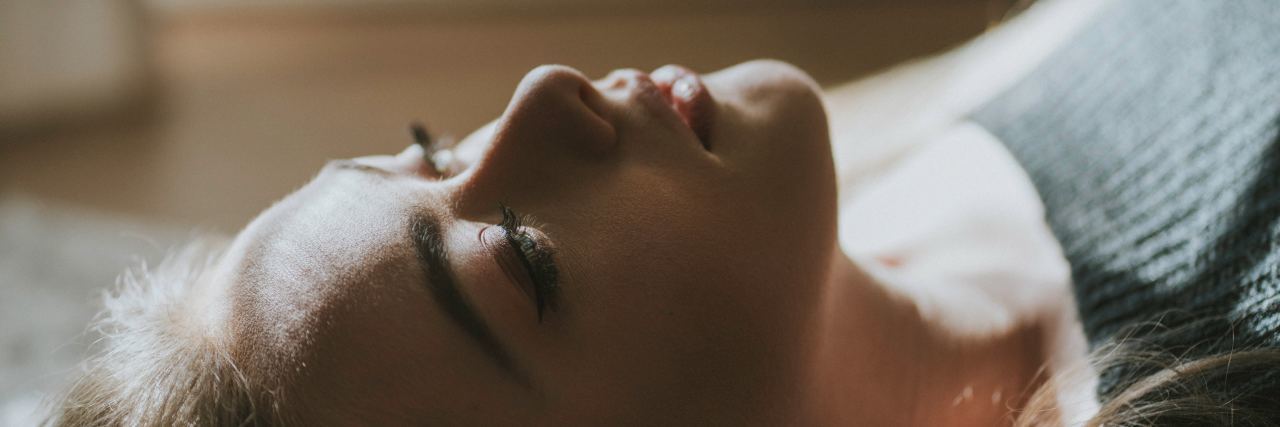 What to Know About Therapy for Childhood Trauma close up photo of woman lying in bed looking up at ceiling with blank expression