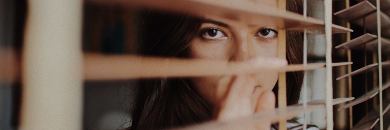 Most Frightening Anxiety Symptoms young woman looking anxious out of window blinds