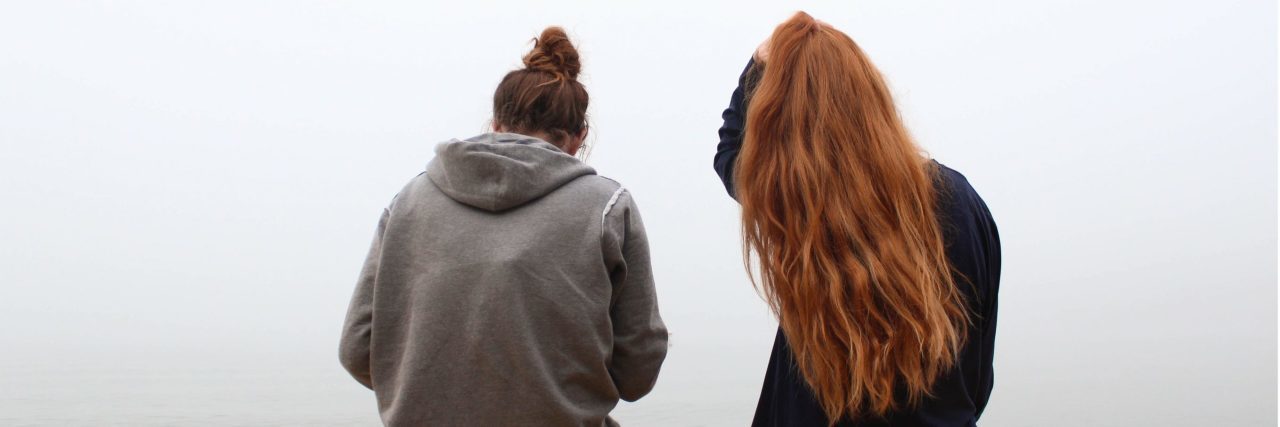 two women sitting by misty lake looking out over water