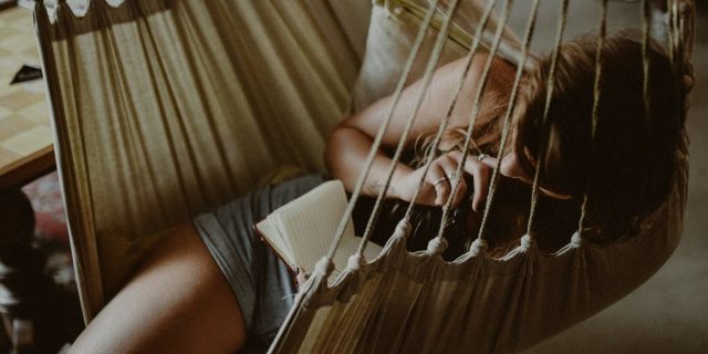 woman reading book while relaxing on hammock
