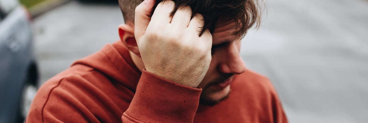 photo of man with hand raised to head in thinking expression and looking away from camera