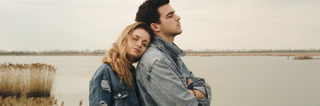 What You Need to Know About Dating Someone With Anxiety couple standing by lake on gray day with woman leaning head on man's back