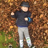 Little boy wearing a medical helmet smiling and laying on a pile of leaves