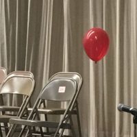 Red balloon at end of row of empty metal chairs before a ceremony