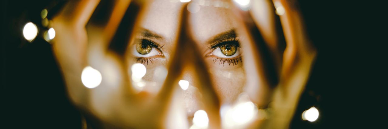 Why I'm Not 'Myself' When I'm Anxious woman covering face with hands and string of lights