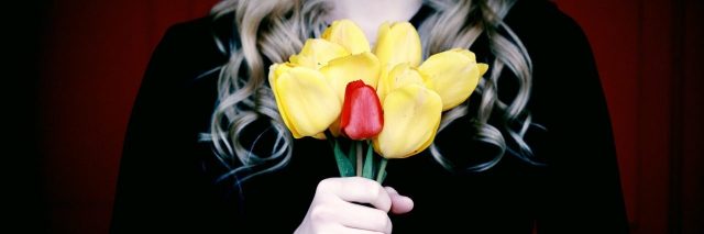 woman clutching yellow tulip flowers with one red flower