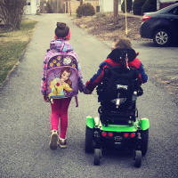 Boy in wheelchair hand in hand with sister as they walk down the street
