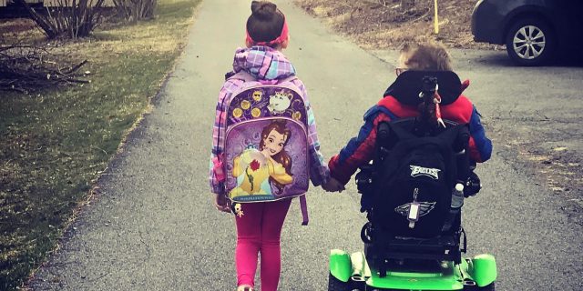 Boy in wheelchair hand in hand with sister as they walk down the street