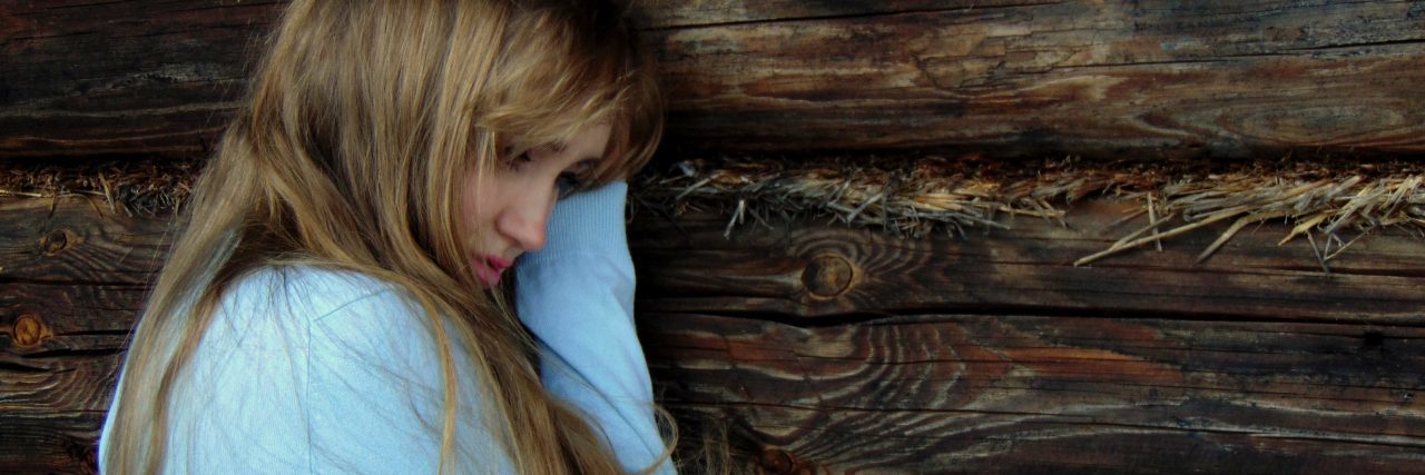 young woman leaning against wood wall looking upset and lonely