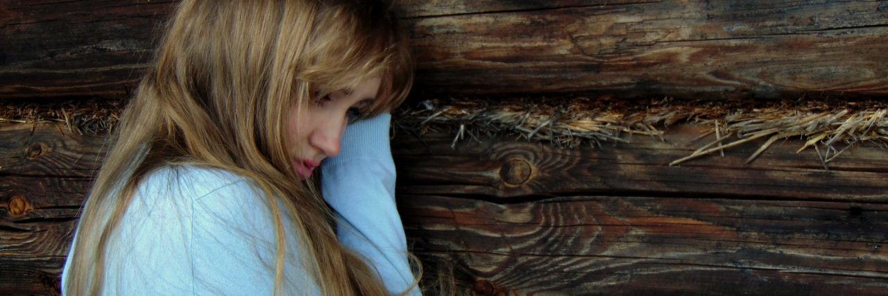 When Anxiety Makes You Hurt People to Push Them Away young woman leaning against wood wall looking upset and lonely