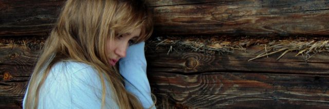 young woman leaning against wood wall looking upset and lonely