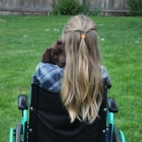 Woman in a wheelchair. In one photo she is alone, in the other she holds a Labrador puppy.
