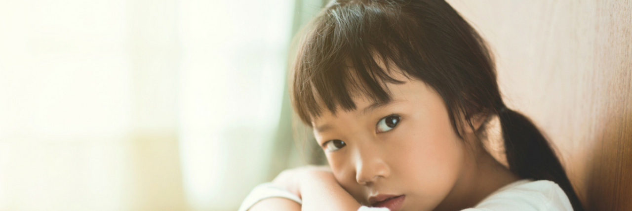 Anxiety Fears That Actually Stem From Childhood Trauma A young girl sitting by a door. Text reads: 30 Anxiety Fears That Actually Stem From Childhood Trauma