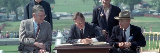 President George Bush signs the ADA as Justin Dart and other distability rights leaders look on.