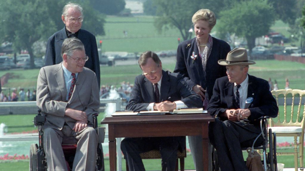 President George Bush signs the ADA as Justin Dart and other distability rights leaders look on.