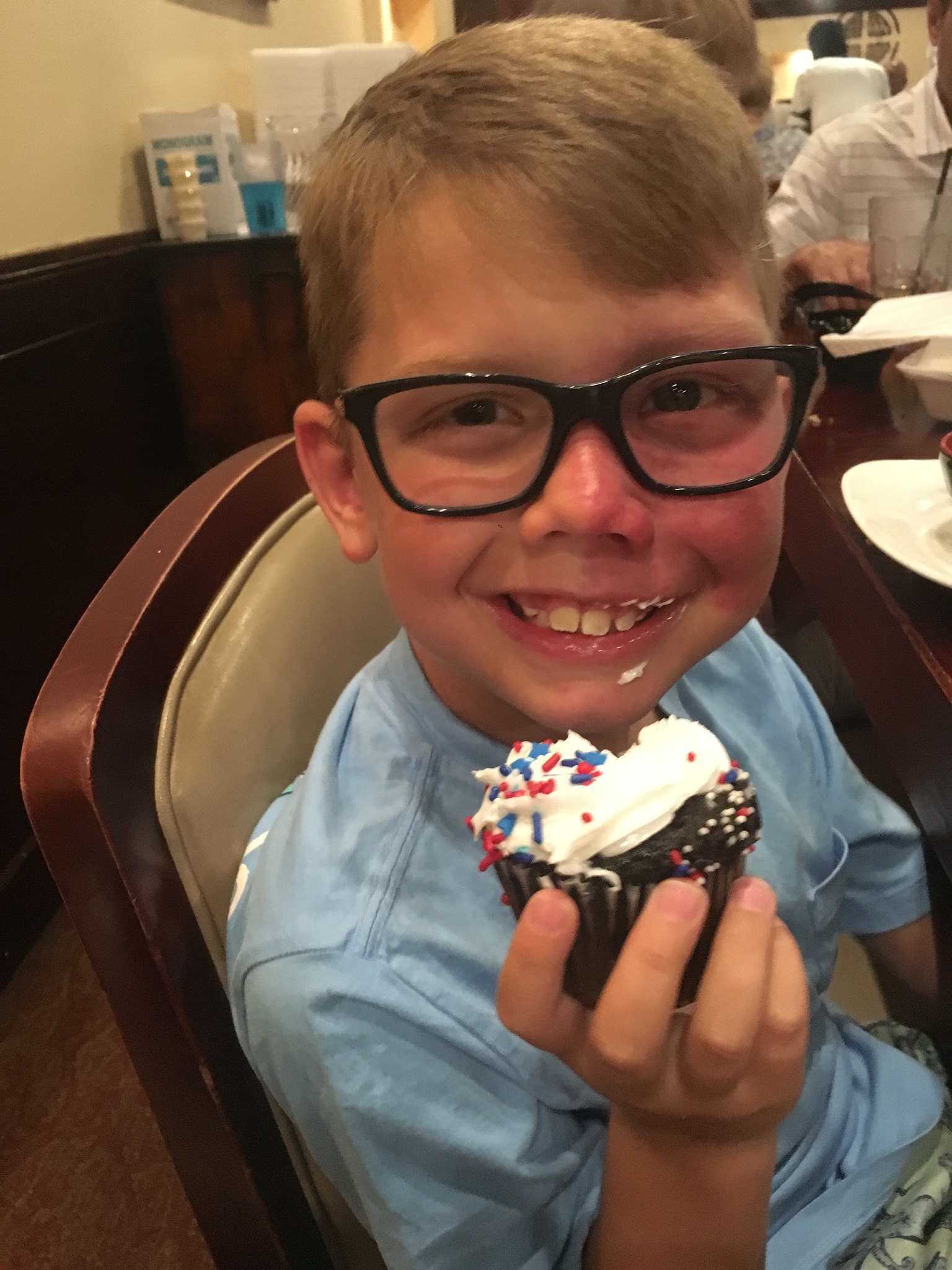 A little boy with a birthmark on his cheek, eating a cupcake.