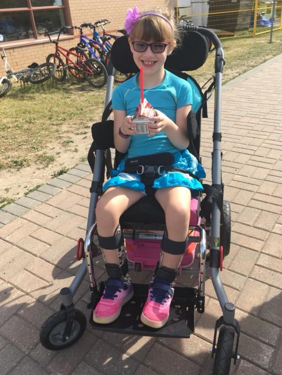 girl in wheelchair wearing leg braces holding small carton with straw