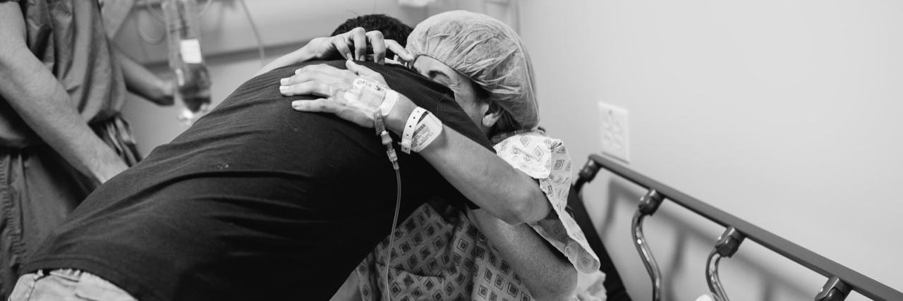 black and white picture of woman in hospital gown hugging a man