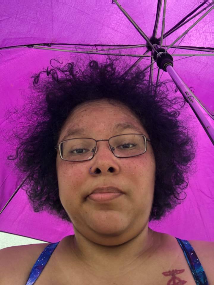 woman sitting outside under a purple umbrella