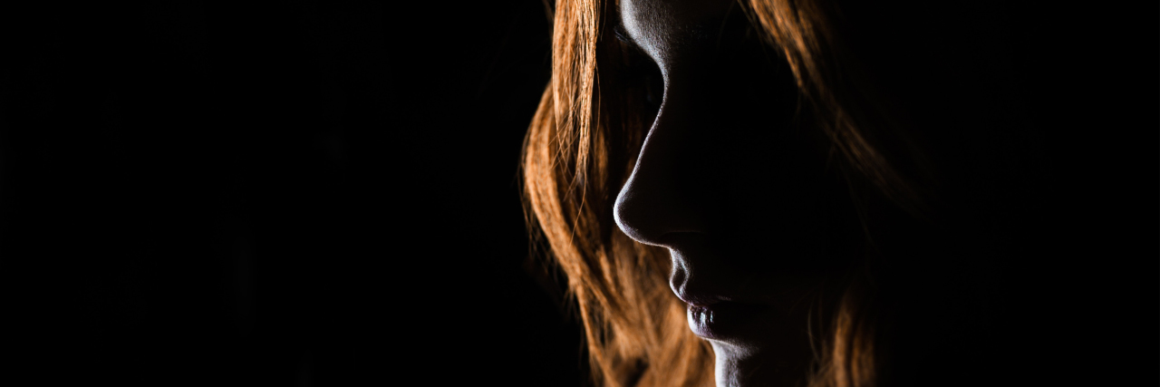 woman with long red hair silhouetted by light against dark background
