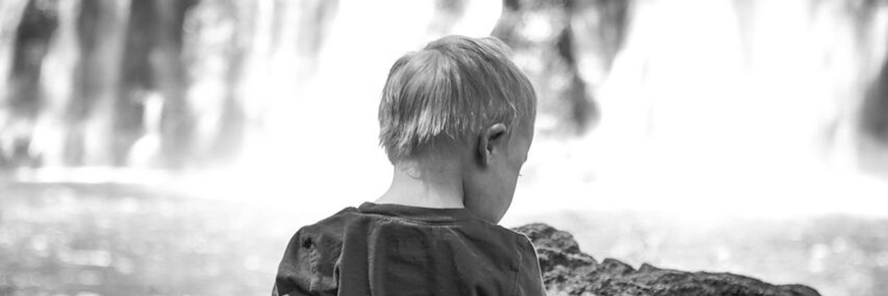 Black and white image of boy facing a waterfall