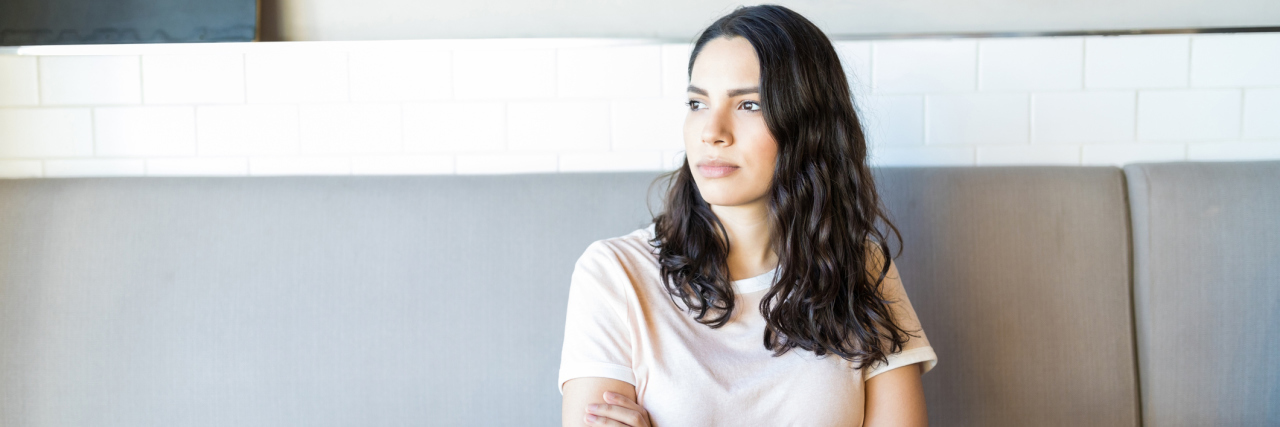 Why I'm Angry as a Disabled Woman With Lupus woman sitting at a table crossing her arms and looking away
