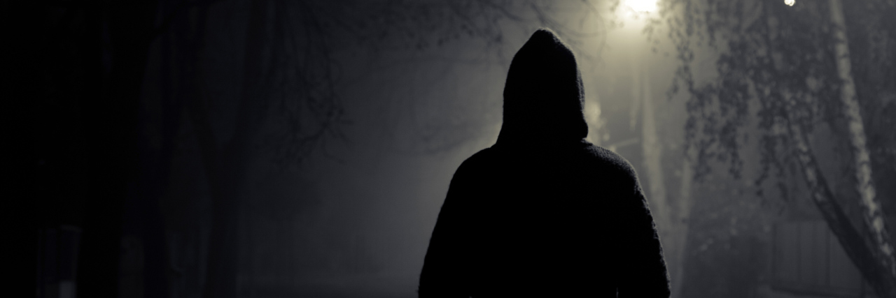 A person walking in the night, wearing a dark hoodie.