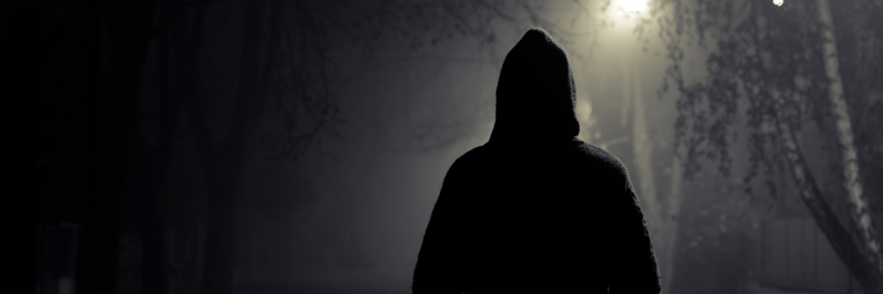 Dear Loved Ones, What You Need to Know About the Thief Inside My Body A person walking in the night, wearing a dark hoodie.