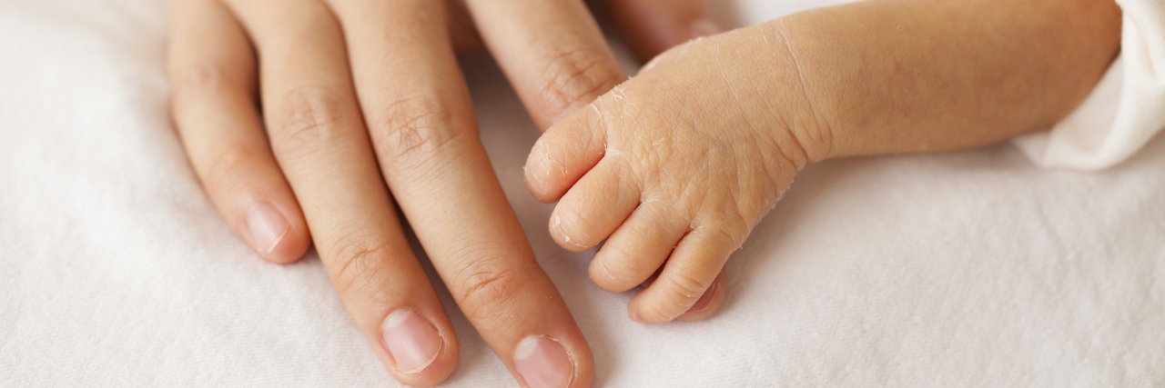 Premature baby hand holding the hands of his mother.