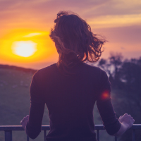 Rear view of young woman admiring the sunset over a field from her balcony