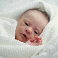 A baby with Down syndrome cuddled up in a white blanket