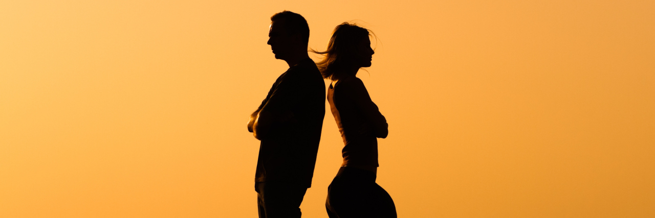 silhouette of man and woman standing facing away from each other with their arms crossed