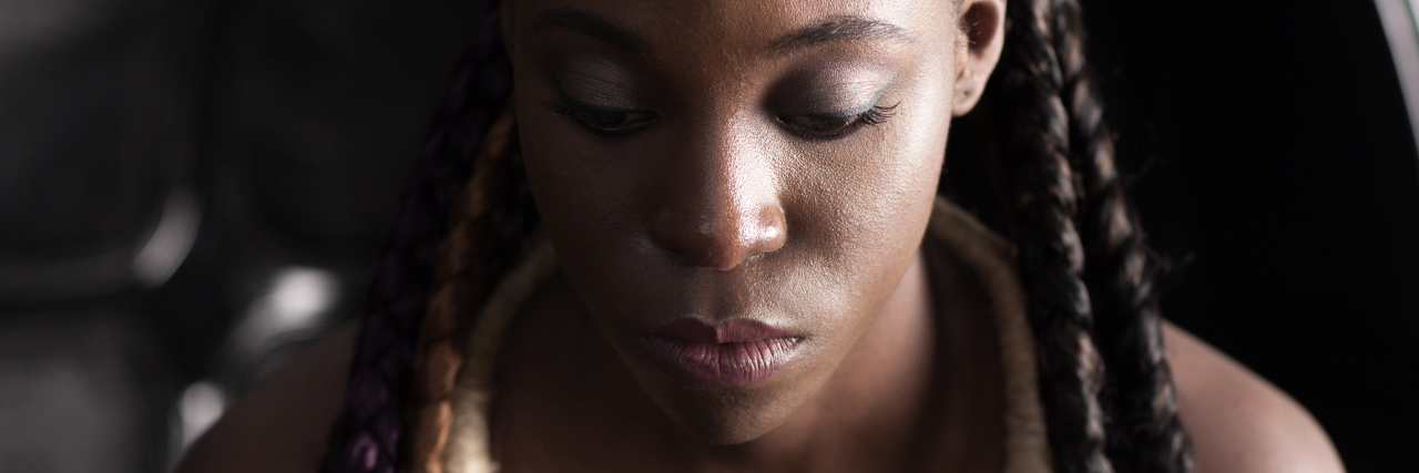 The Invisible Medical Hoops That Black Women Have to Jump Through A woman looking towards the ground with a serious facial expression.