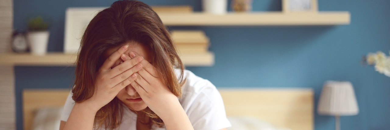 25 Surprising Physical Symptoms of Migraine Woman holding head in her hands sitting in bed