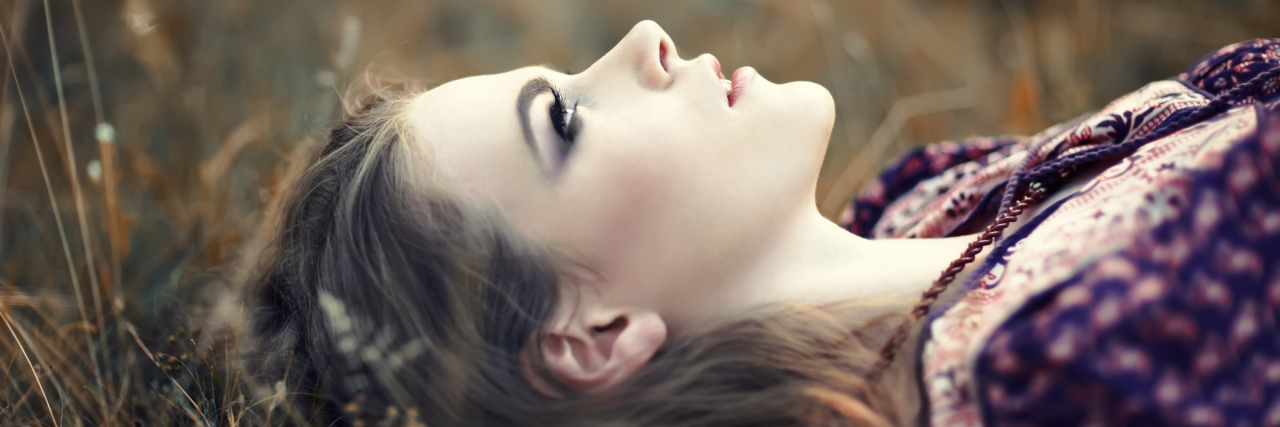A portrait of a woman laying on grass, looking up to the sky.