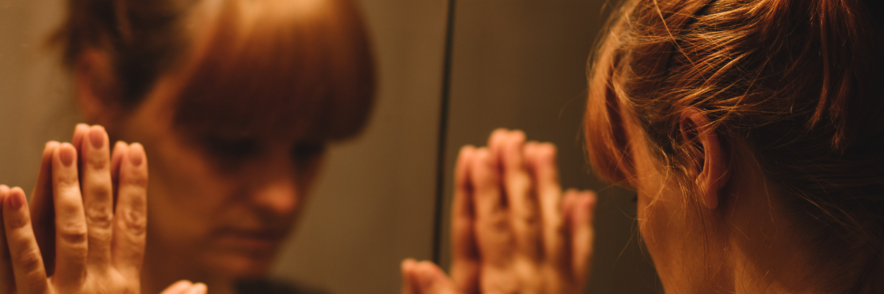 Why I Experience 'Flare Fear' on My Good and Bad Health Days A woman looking into the mirror, uncertain.